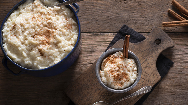 A big crock of rice pudding next to a smaller bowl sprinkled with cinnamon.
