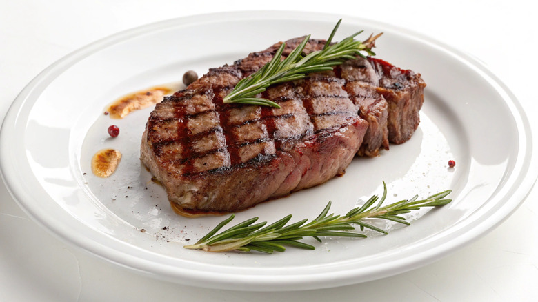 A steak with grill marks and herbs on a white plate.