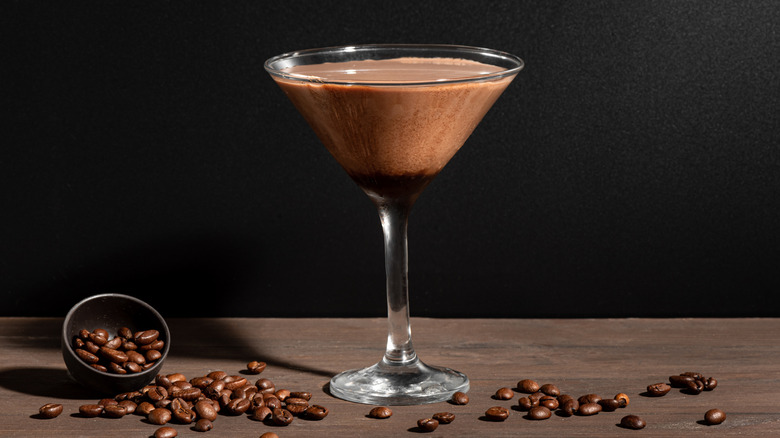 Espresso martini in a glass surrounded by coffee beans.