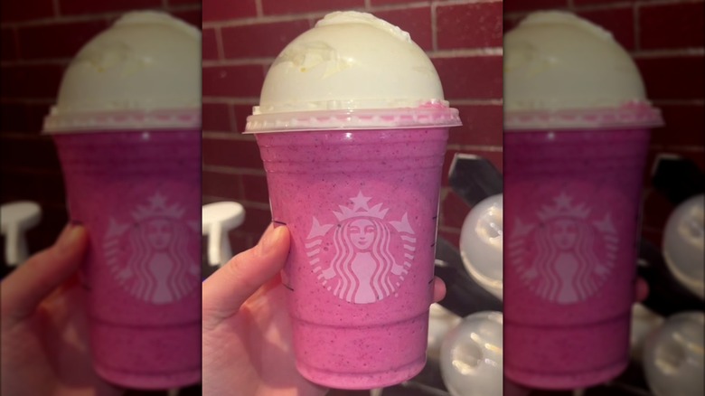 Someone holding a hot pink Starbucks drink in front of a brick wall