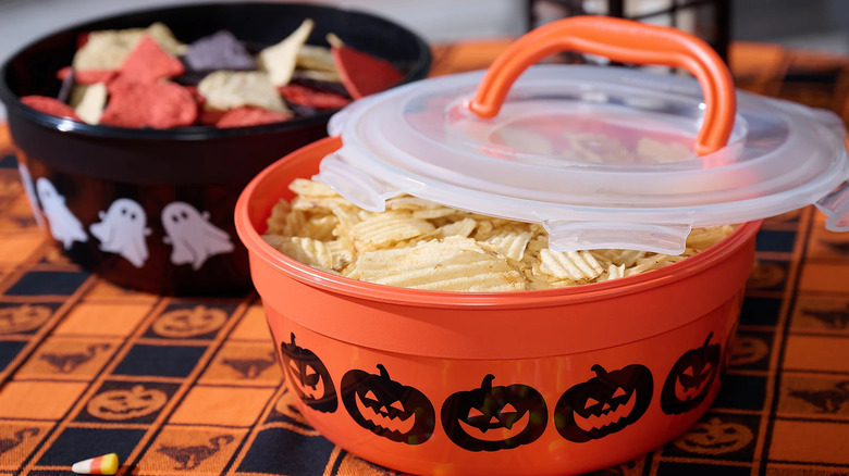 Two LocknLock Halloween candy bowls sit on a table, a pumpkin-decorated bowl with ruffle chips and a ghost-decorated bowl with tri-colored tortilla chips.