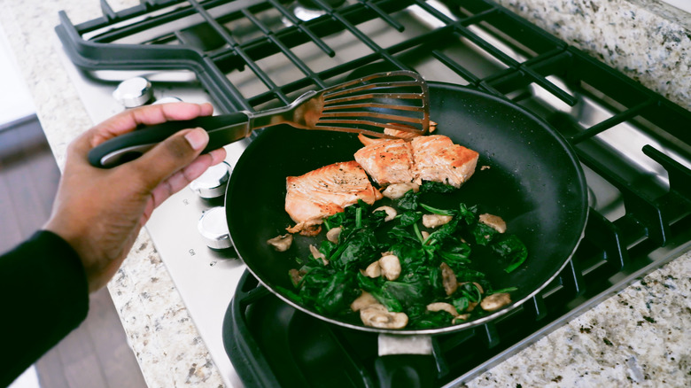 Close up of a someone cooking salmon and spinach on a stove top using a fish spatula