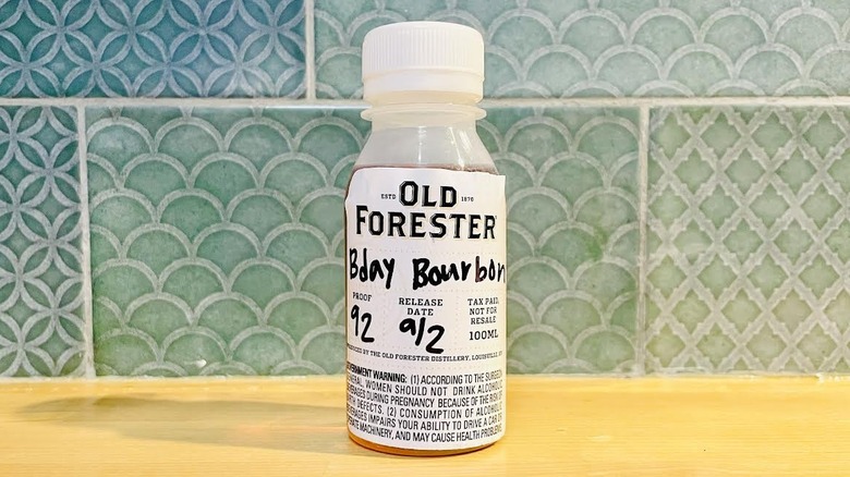Sample bottle of Old Forester Birthday Bourbon 2025 on wooden counter with aqua-colored backsplash