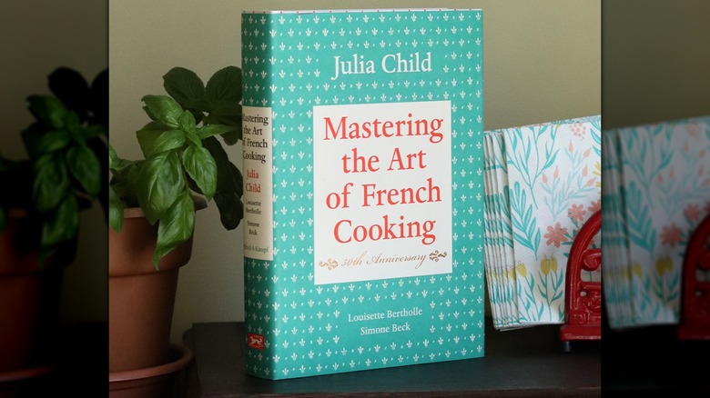"Mastering the Art of French Cooking" beside a potted plant and a set of paper napkins
