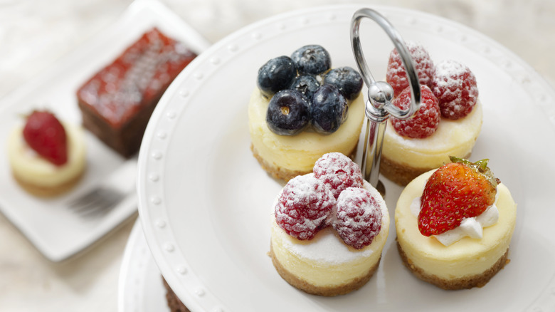 A fancy tray with four mini cheesecakes, each one garnished with different berries.