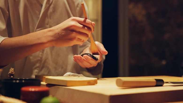 A man's hand brushing a piece of fish with a wooden brush
