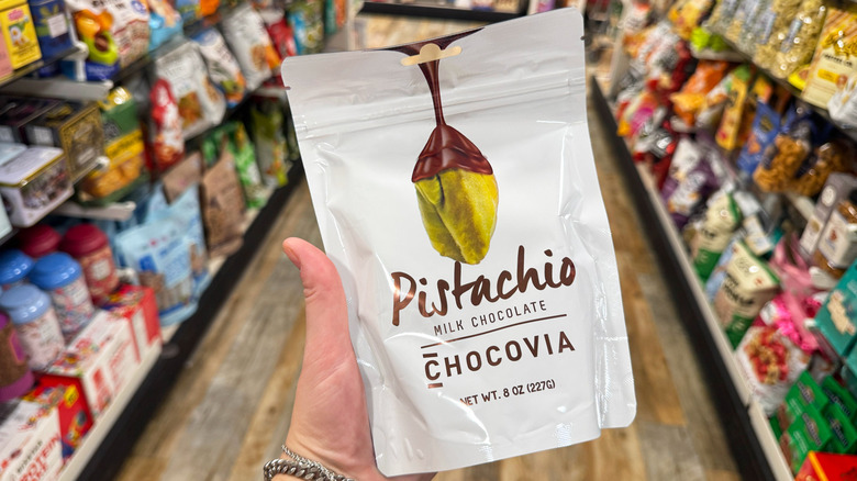 A hand holds up a bag of chocolate covered pistachios