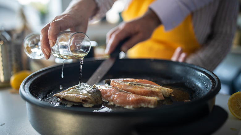 White wine being poured into a pan with fish.