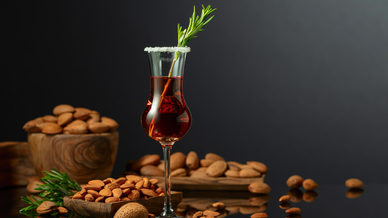 A glass of amaretto sits against a dark background surrounded by almonds