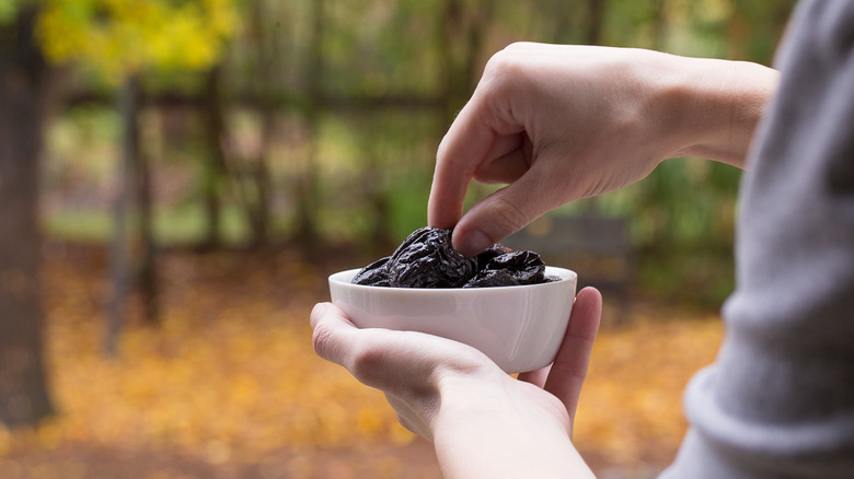 A woman's hand picks up a prune from a white bowl
