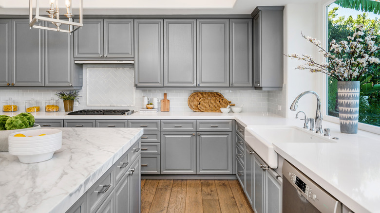 A bright kitchen with grey cabinets and marble countertops