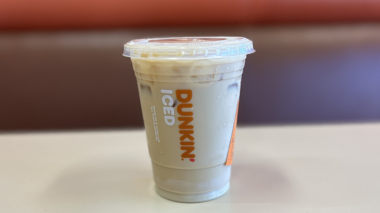 Pistachio iced coffee on a white table with the plastic lid on top