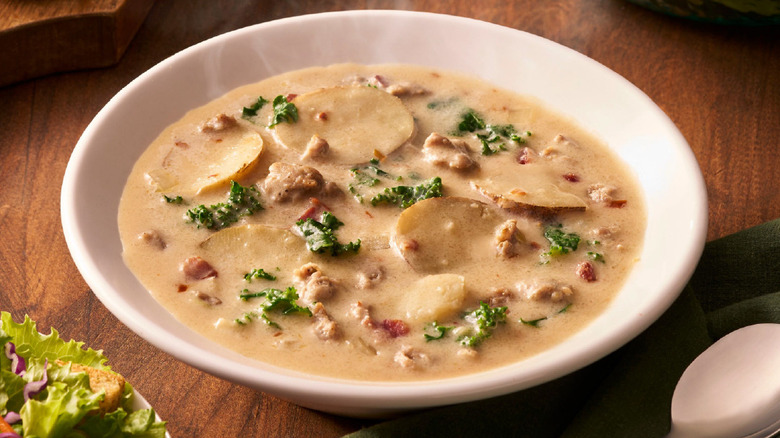 A bowl of Olive Garden's zuppa toscana rests next to a bowl of salad