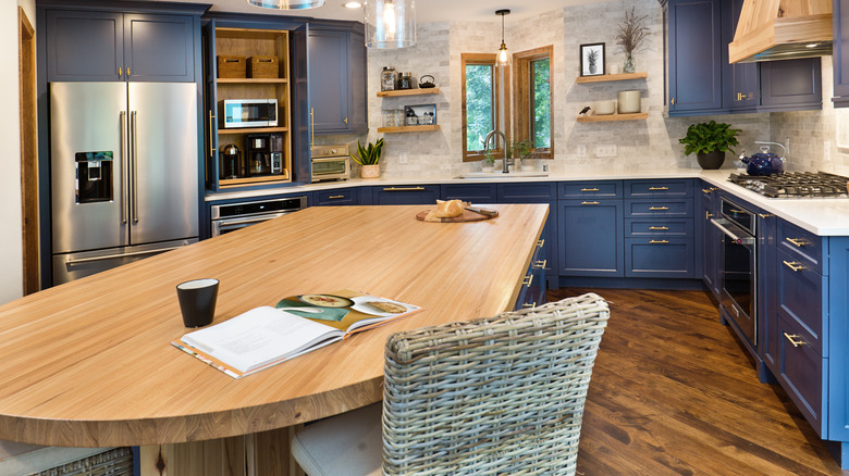 A wood-topped kitchen island with one rounded end is situated in a modern kitchen with blue cabinetry