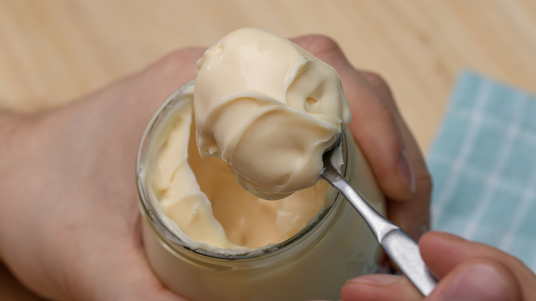 hands holding a jar and a spoonful of mayonnaise