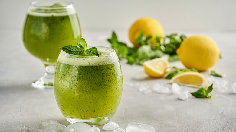 Limonana, Middle Eastern lemonade, in two glasses, topped with mint, next to sliced lemons, fresh mint, and ice cubes