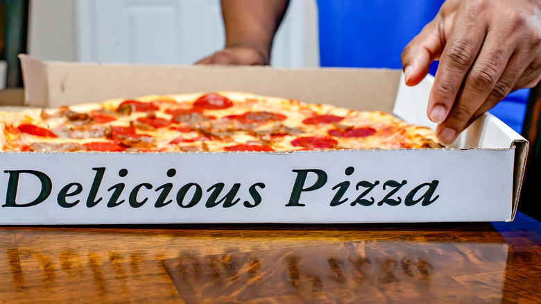 A person reaching into an open box of pizza