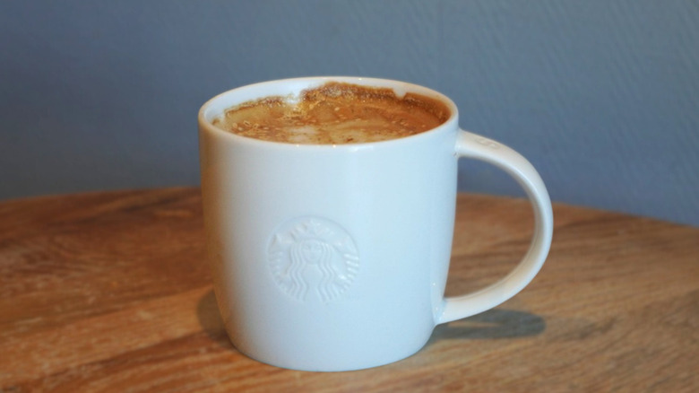 Pecan Oatmilk Cortado on a wooden table in front of a gray wall