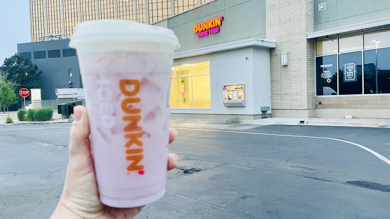 Hand holding Sabrina's Strawberry Daydream Refresher in front of Dunkin' drive-thru