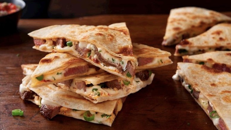 Pieces of quesadillas piled on a table displaying steak and cheese filling
