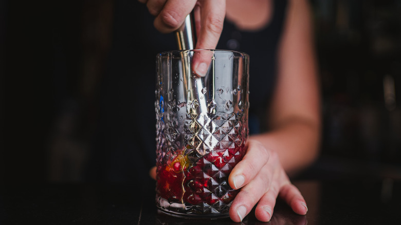 A bartender muddles fruit in a cocktail glass