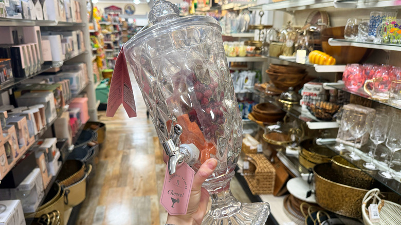 A hand holds up a beveled drink dispenser in a HomeGoods aisle