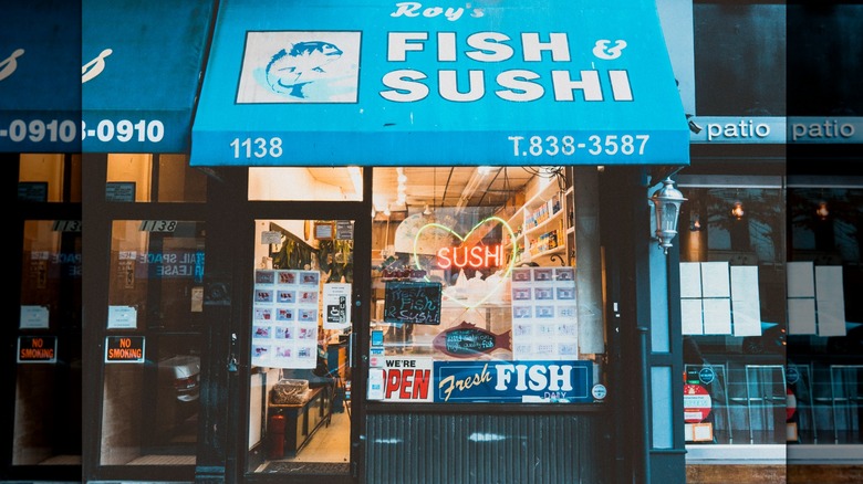 The exterior of Foy's Fish Market, a blue awning and a neon saying that says "sushi"