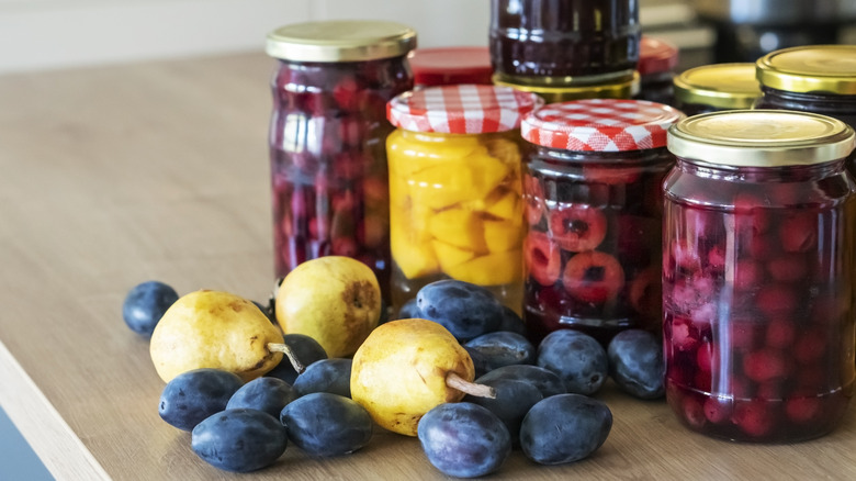 Pears and plums in front of jars of fruit