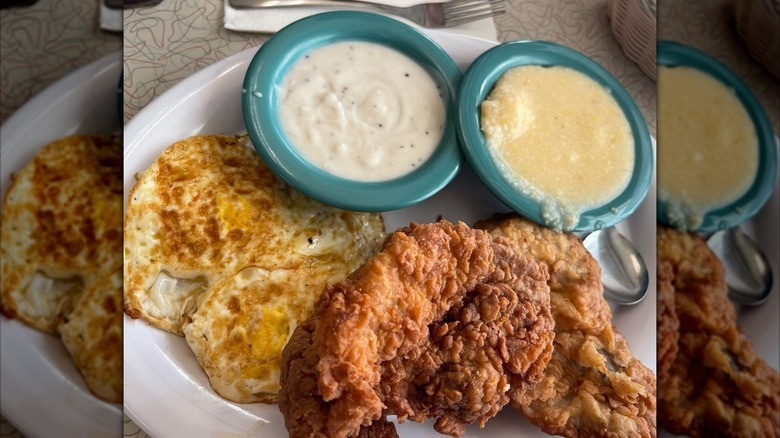 Fried eggs and a mess of fried chicken sit side by side next to thick white gravy and grits