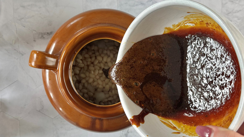 pouring molasses seasoning into dutch oven with beans