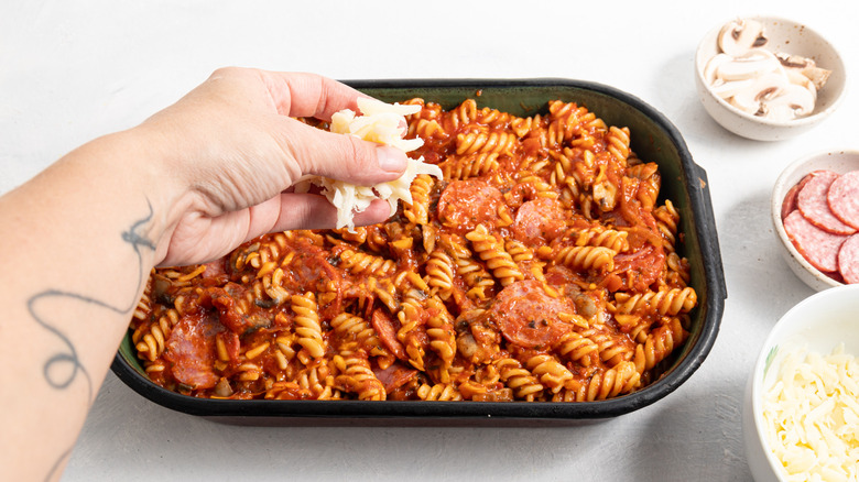 Sprinkling shredded cheese on top of fusilli pasta bake