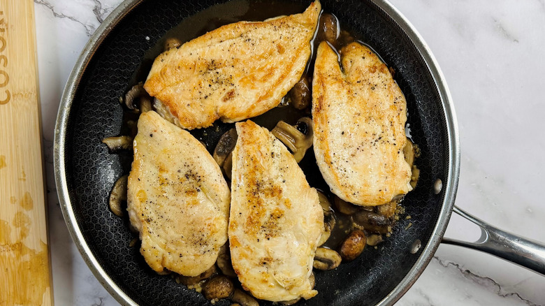 Seared chicken on top of mushrooms and sauce in frying pan