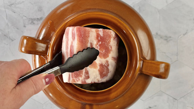 adding salt pork to dutch oven with tongs