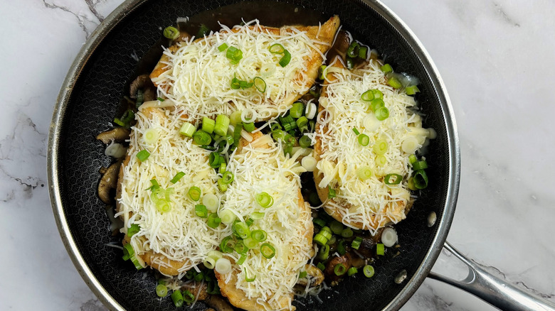 chicken topped with cheese and scallions in frying pan