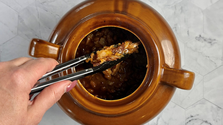 breaking up cooked salt pork in dutch oven with tongs