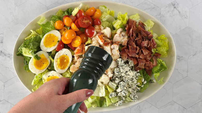 cracking black pepper over cobb salad