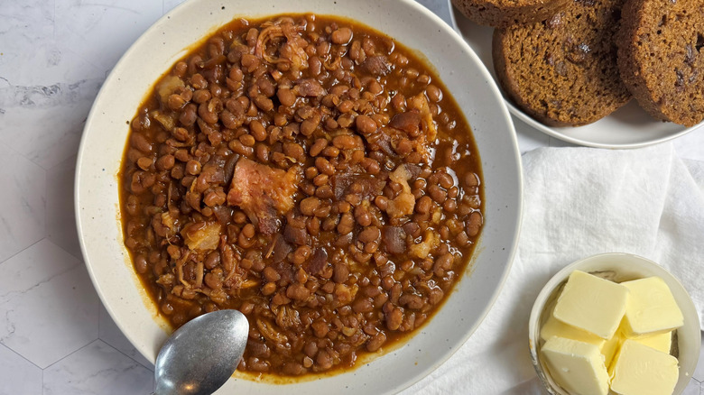 bowl with baked beans and two spoons next to cubed butter and bread