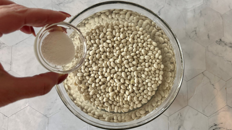 adding salt to bowl with beans and water