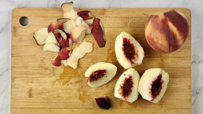 whole and quartered peach with a peach pit and peels