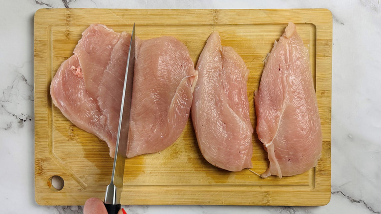 hand cutting raw chicken on wooden cutting board