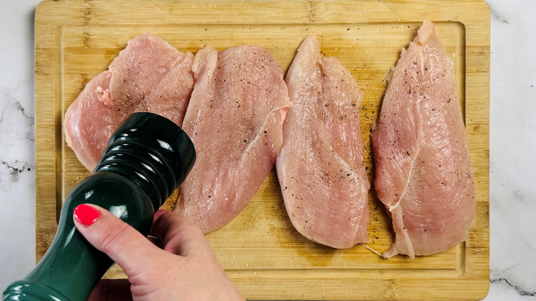hand holding pepper grinder over raw chicken
