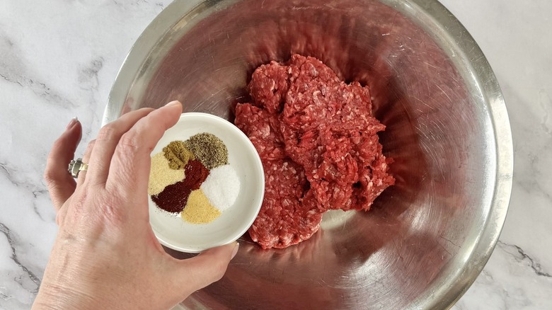 hand holding seasonings above a bowl of ground beef