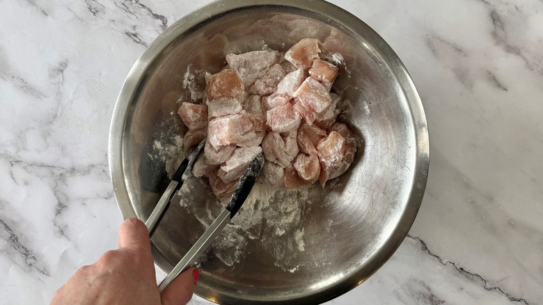 using tongs to toss chicken with flour in bowl
