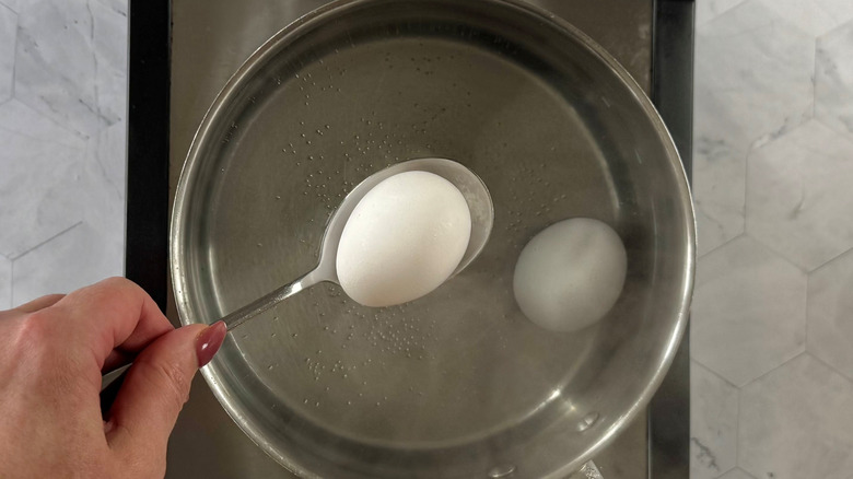 dropping egg on spoon in saucepan with water