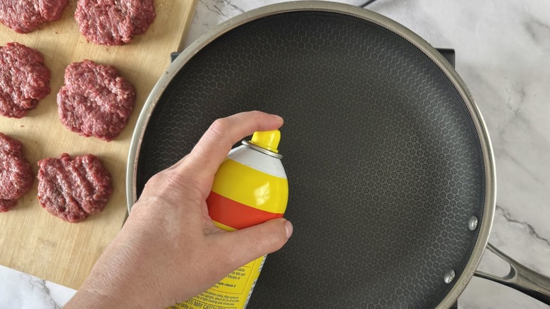 hand squirting frying pan with cooking spray