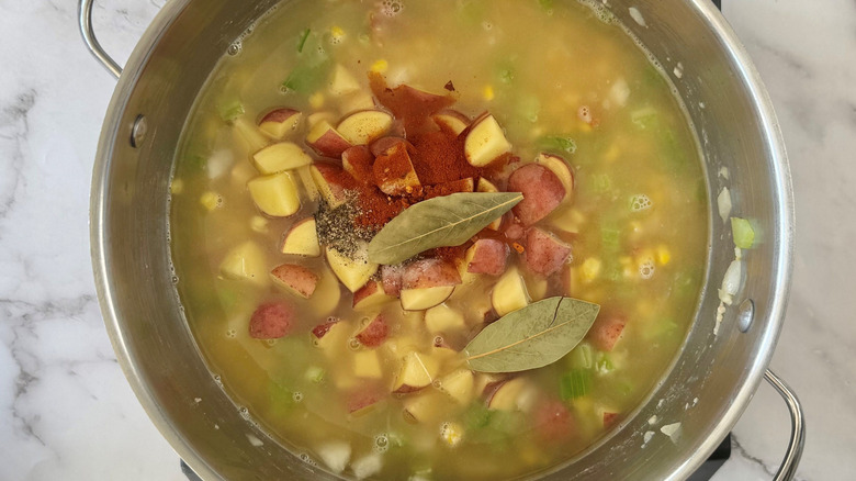 Large soup pot with broth, mixed veggies, seasonings, and bay leaves on top
