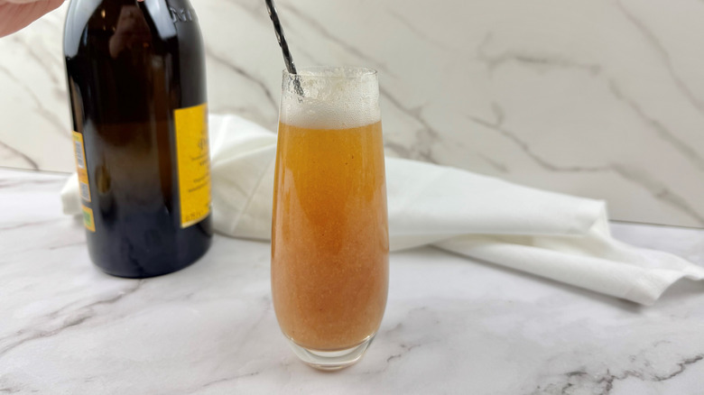 hand stirring orange-colored cocktail in a drinking glass