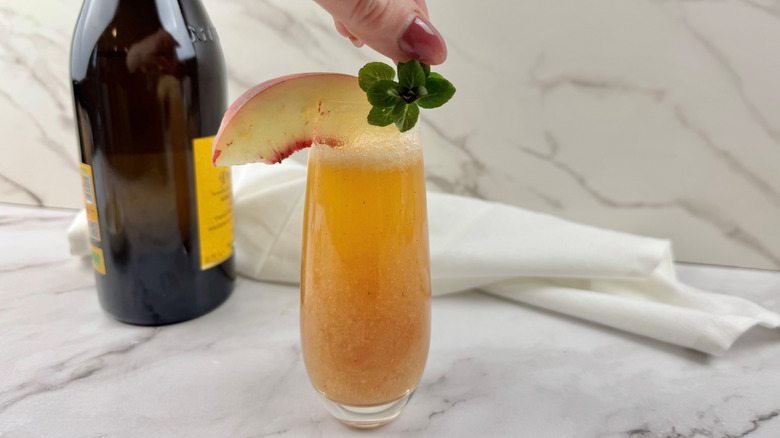 hand holding a piece of mint over an orange-colored cocktail in a drinking glass