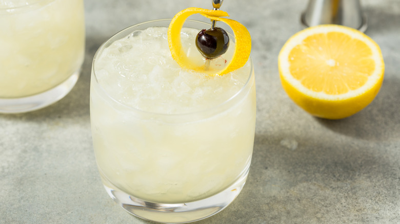 A cold Saturn cocktail made with gin and orgeat with a cherry and ringed lemon peel garnish