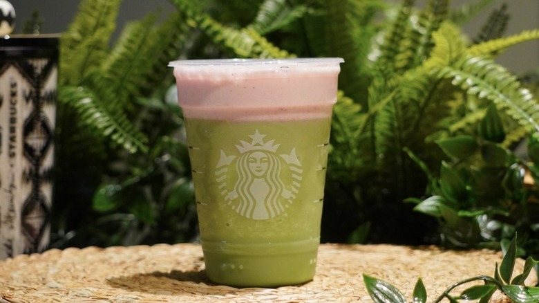 Strawberry Matcha Strato Frappuccino placed on a woven placemat in front of greenery